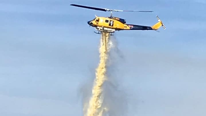 A yellow firefighting helicopter drops a load of water.