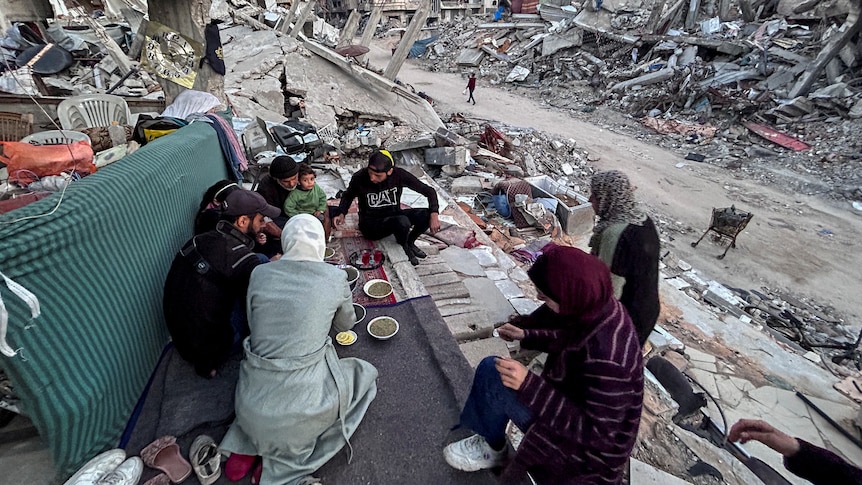 A family breaks bread amid rubble in Gaza.