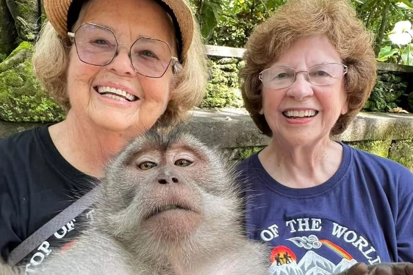 Two elderly ladies sitting a taking a selfie with a monkey 