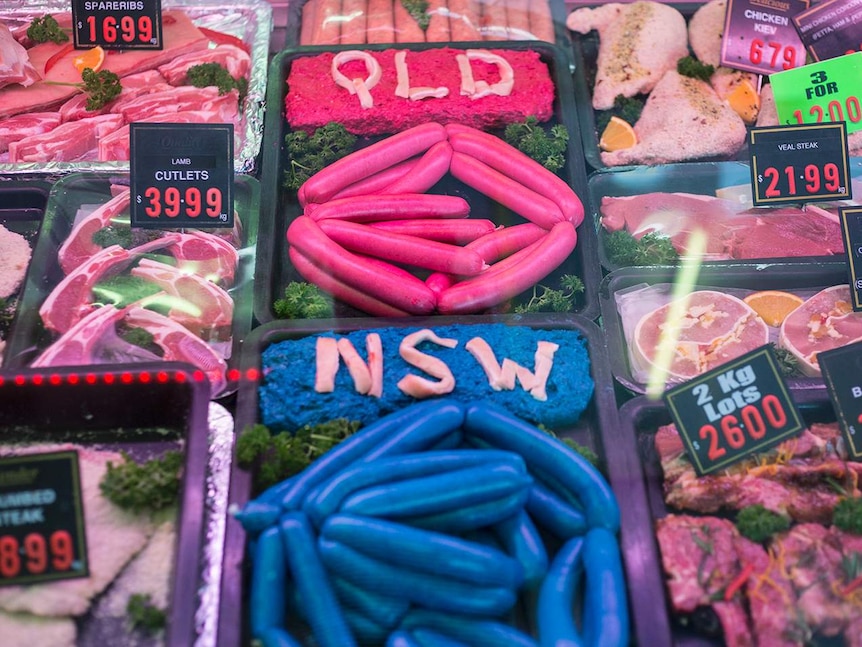 A butcher's cabinet has various meats, including two trays of blue and maroon sausages for State of Origin