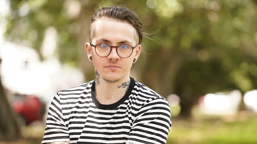 A close up of a man, Az Cosgrove. He is wearing a striped shirt and wearing glasses.