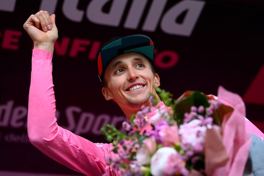 Jay Hindley sonríe y sostiene un ramo de flores con la otra mano levantada en el aire