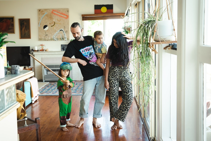 A man and a woman standing in their kitchen, with two kids