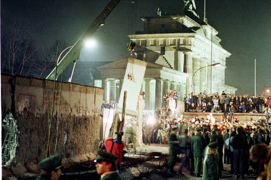 A big section of the Berlin Wall is lifted by a crane as East Germany starts to dismantle the wall near the Brandenburg Gate.