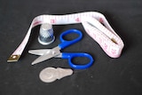 A measuring tape, thimble and sewing scissors sit on a dark surface