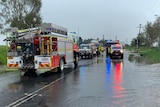 A few fire trucks and police vehicles at the edge of a flooded road
