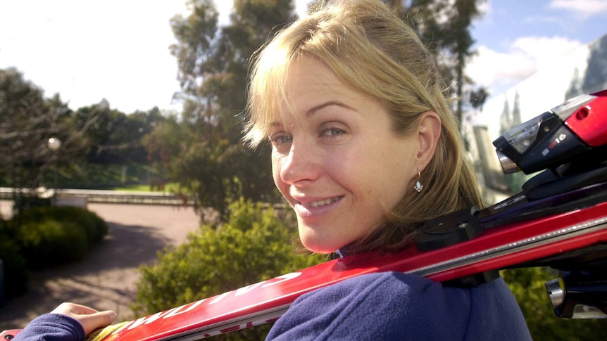 A woman holds a pair of skiis over her shoulder