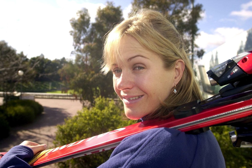 A woman holds a pair of skiis over her shoulder