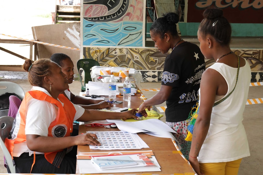 A woman dips her hand in a blue pot of ink as her identity is checked by electoral officials.