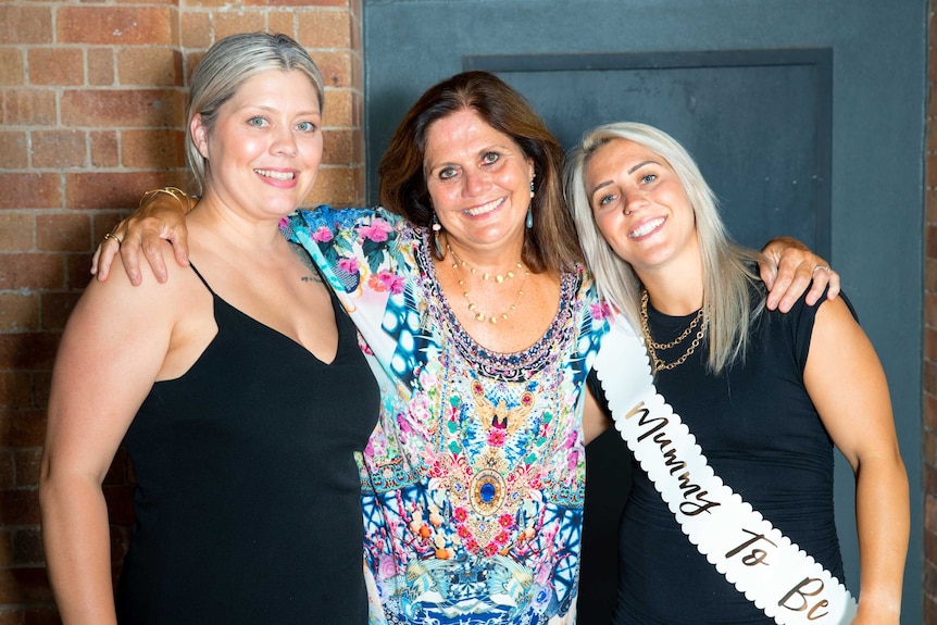 Three women hold their arms around each other and smile.