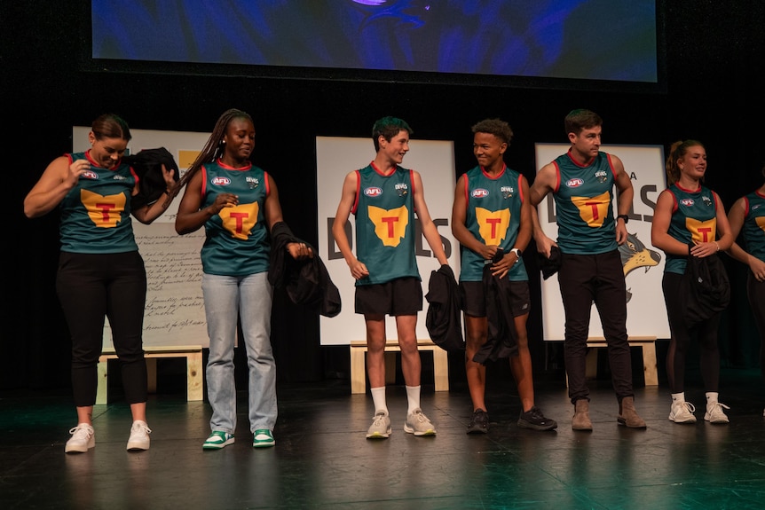 Seven young footballers wear Tasmania guernseys on stage