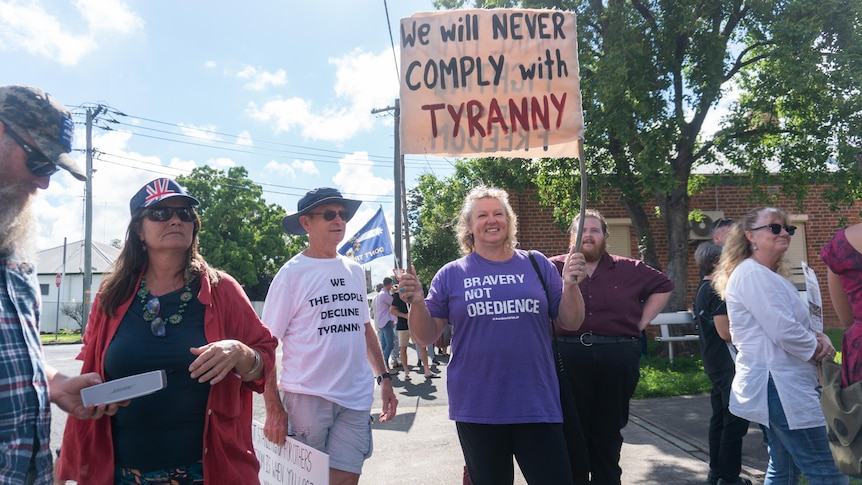 A woman holding a sign reading "we will never comply with tyranny".