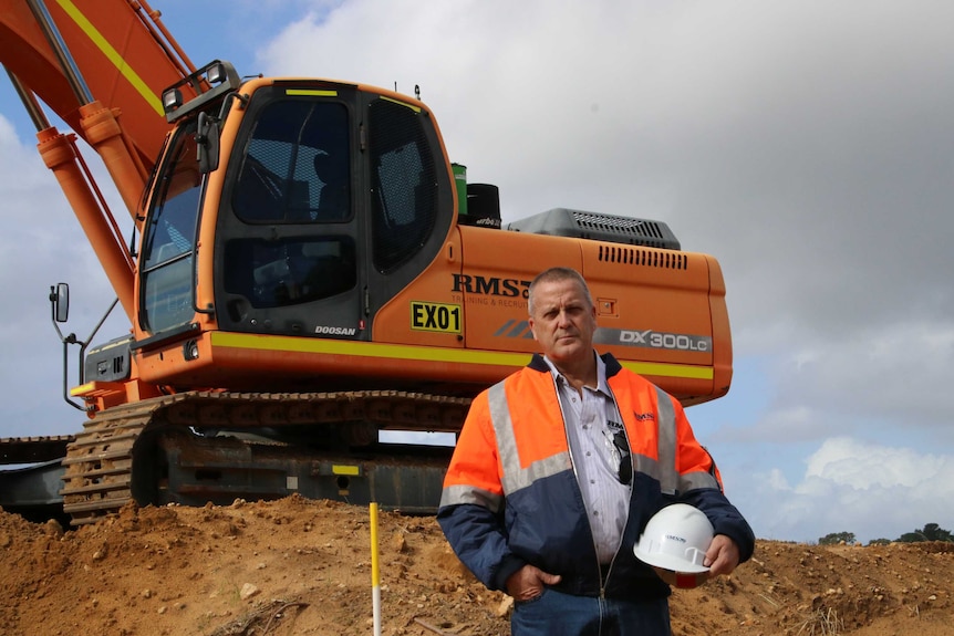 Graeme Richards wearing a high visibility jacket and standing in front of heavy machinery.