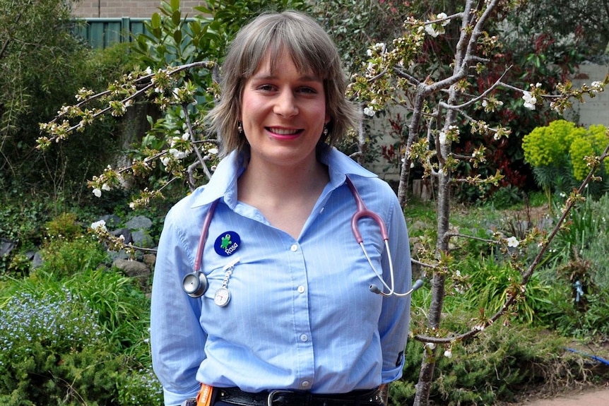 A woman stands with her blue nurse's uniform and stethoscope around her neck. 