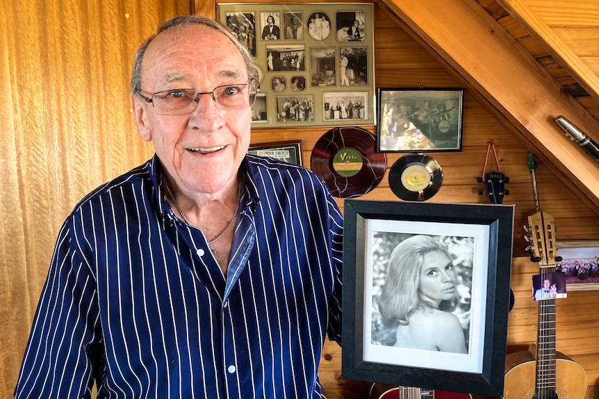 A smiling man in his 80s holds a black and white photo of a beautiful young woman.