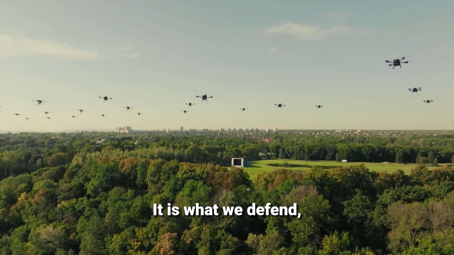 Almost two dozen drones flying over a green city park.