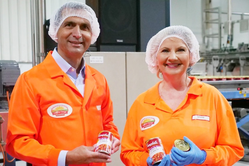A man and woman dressed in orange hi-vis workwear in a can making factory