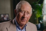 Prince Charles sits in a living room, with family photos in the background.