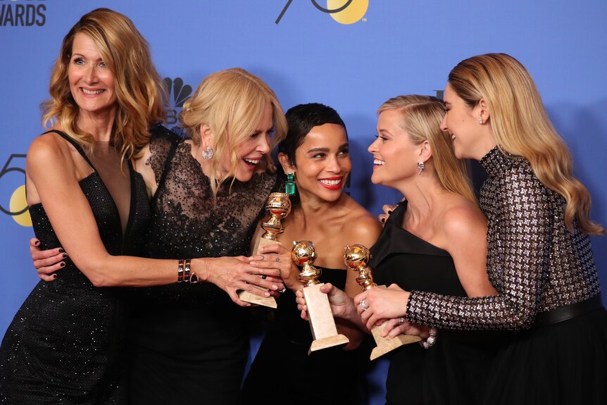 The five female stars of the show laugh and smile as they pose for pictures together with their three gold trophies.