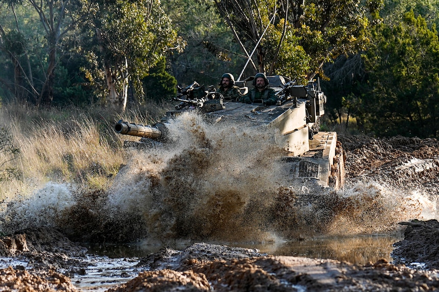 A tank drives through muddy water. 