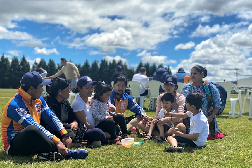 People from Nepal in cricket gear sit on the grass with family members