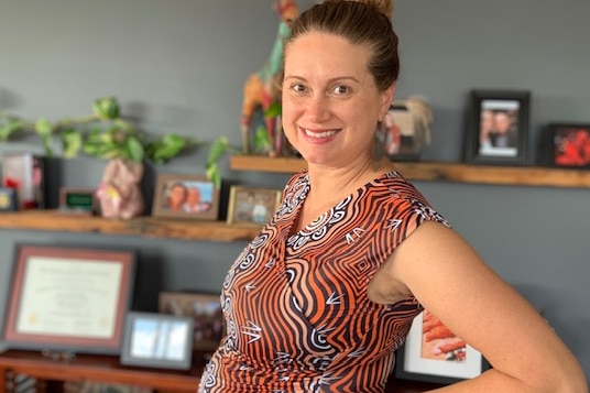 Njamal woman Dee Malek standing side-on in an office with her pregnant belly visible in a dress with First Nations print