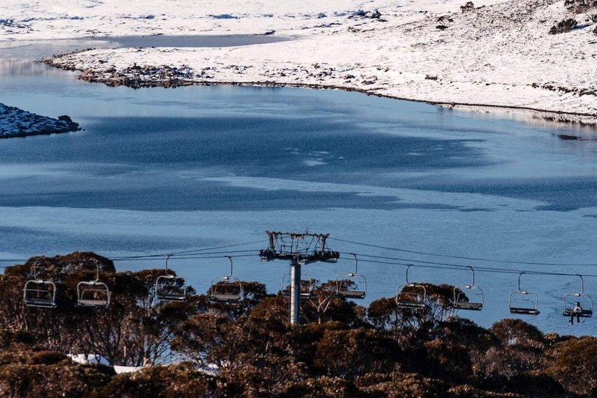 A photo of Falls Creek with some snow, a body of water and some chairlifts.