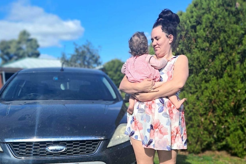 a photo of a woman holding baby in front of car