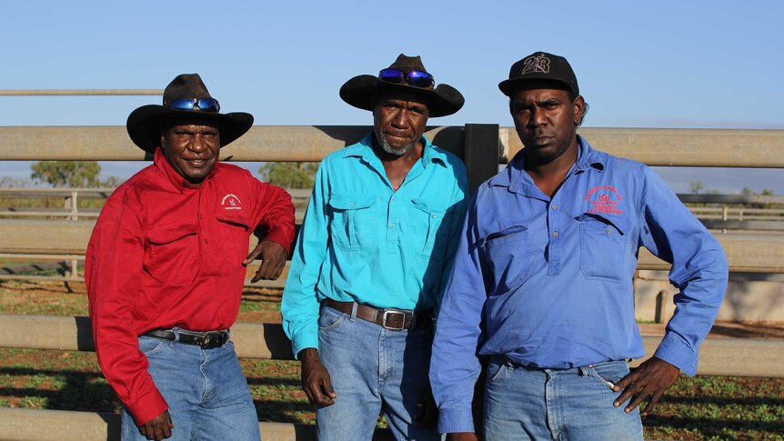 three men in hats standing next to a cattle yard