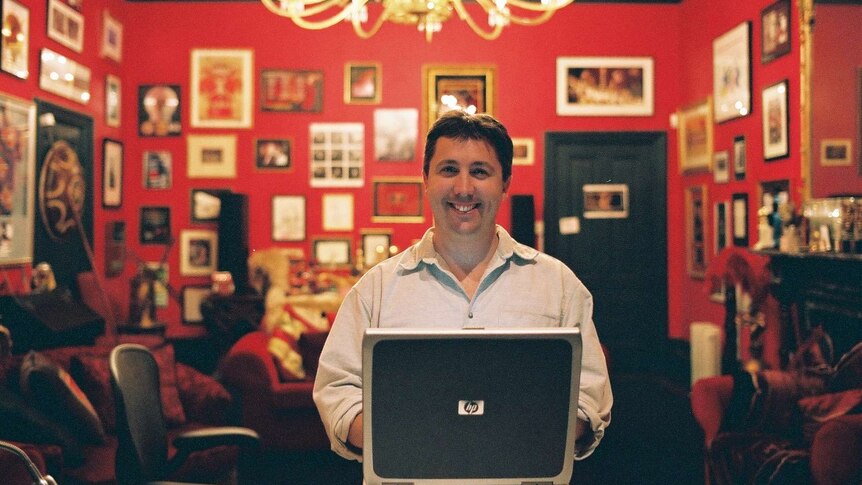 Man with laptop sitting in red drawing room with lots of artwork on walls