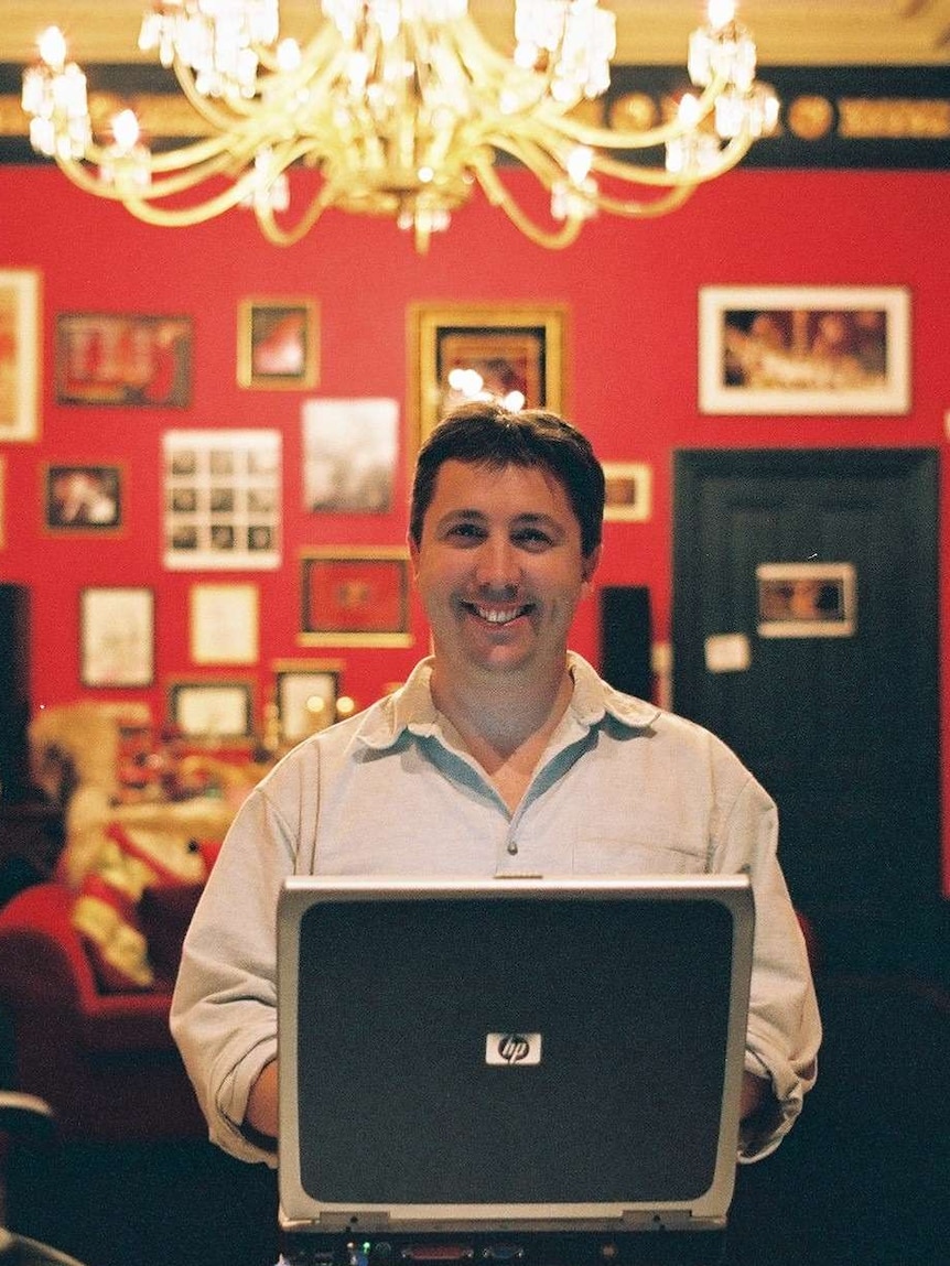 Man with laptop sitting in red drawing room with lots of artwork on walls