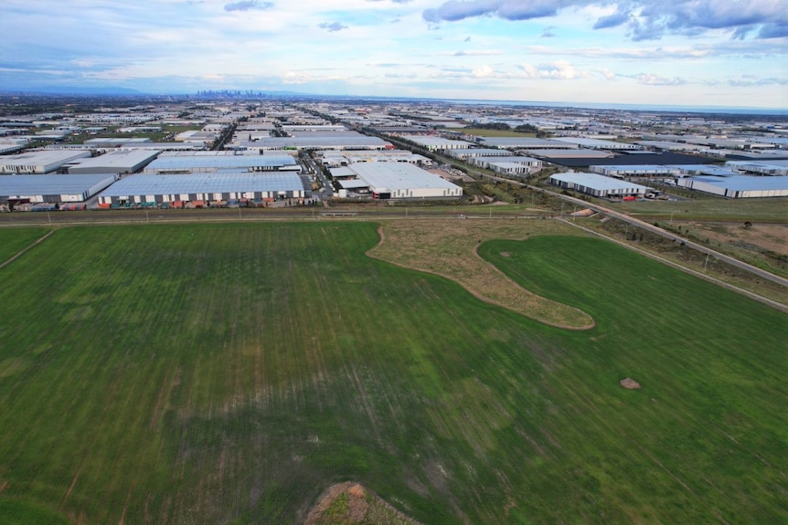 A drone picture of a large field surrounded by warehouses and the city in the background.