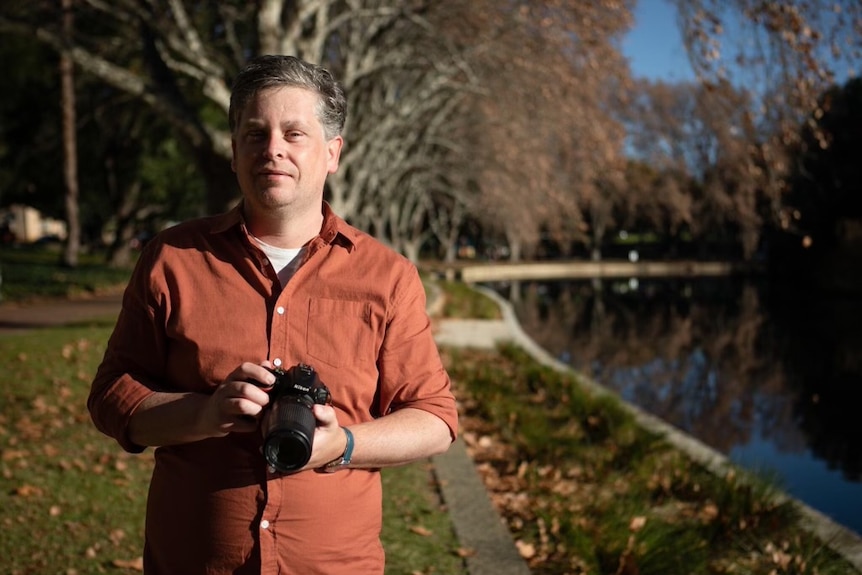 Man in red button up shirt holds camera