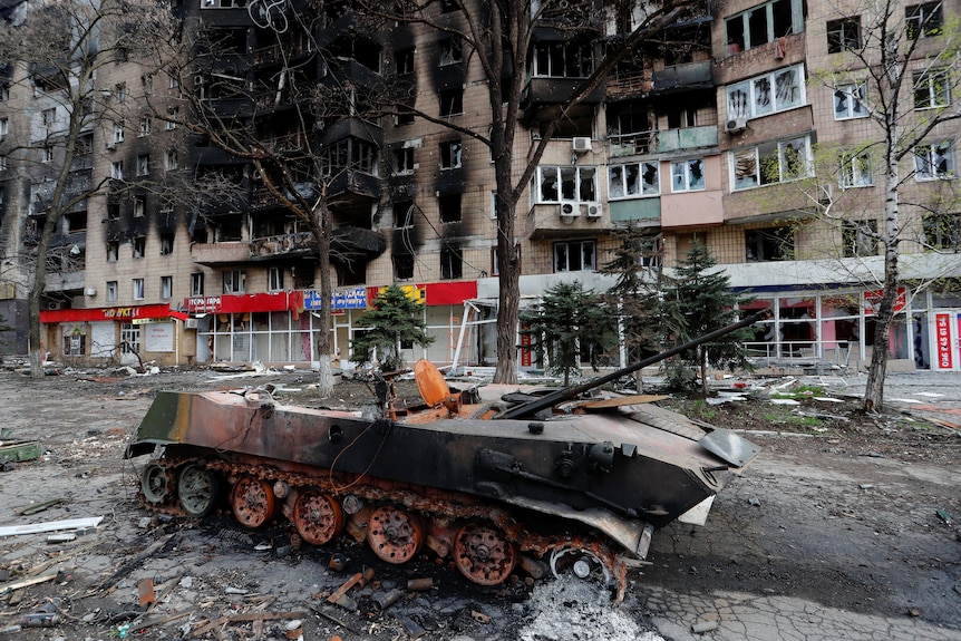 A destroyed tank in the middle of a deserted apartment lined street.