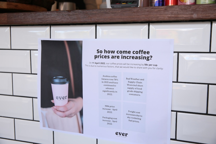 A sign showing why a cafe is pushing up coffee prices, stuck to tiled wall