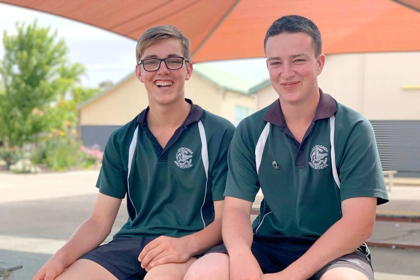 Two young males sitting on a bench next to each other and laughing.