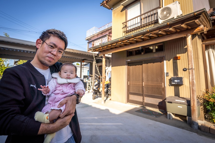 Un primer plano de un hombre con su bebé afuera de una casa en Japón.