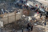 Groups of people stand among debris looking at a hole in the ground after an Israeli airstrike in the northern Gaza Strip.