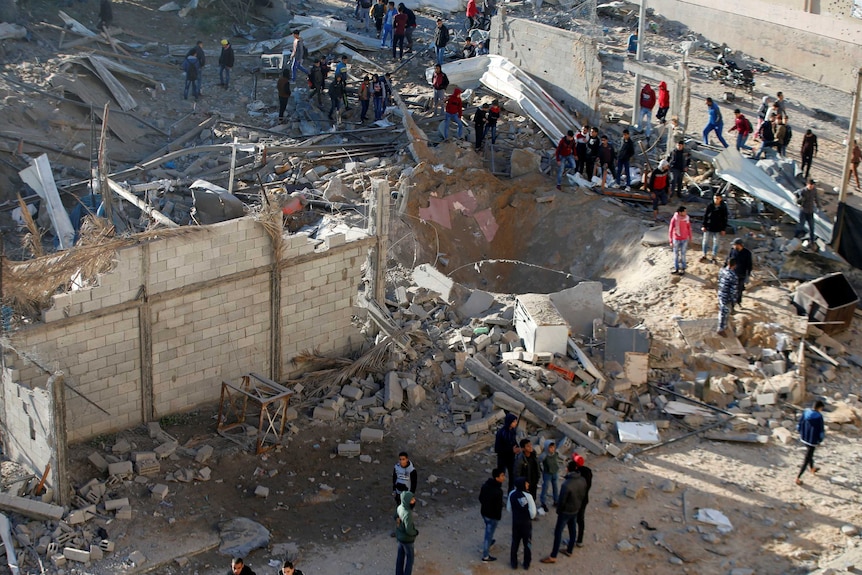 Groups of people stand among debris looking at a hole in the ground after an Israeli airstrike in the northern Gaza Strip.