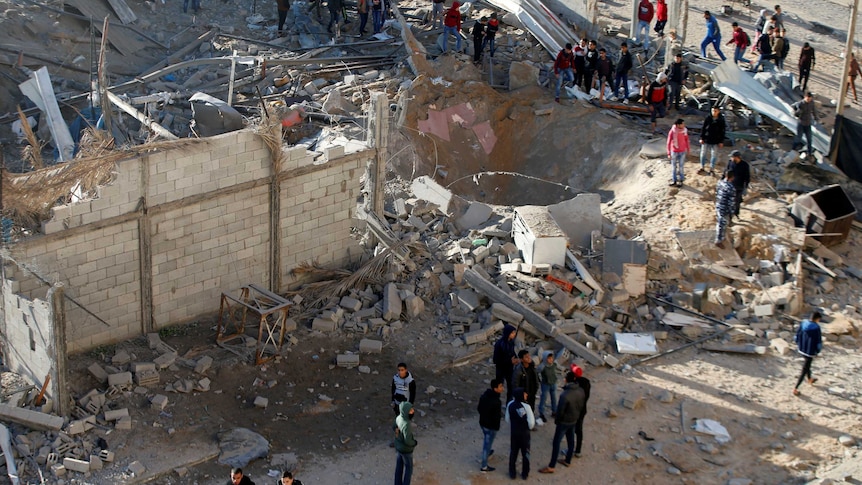 Groups of people stand among debris looking at a hole in the ground after an Israeli airstrike in the northern Gaza Strip.