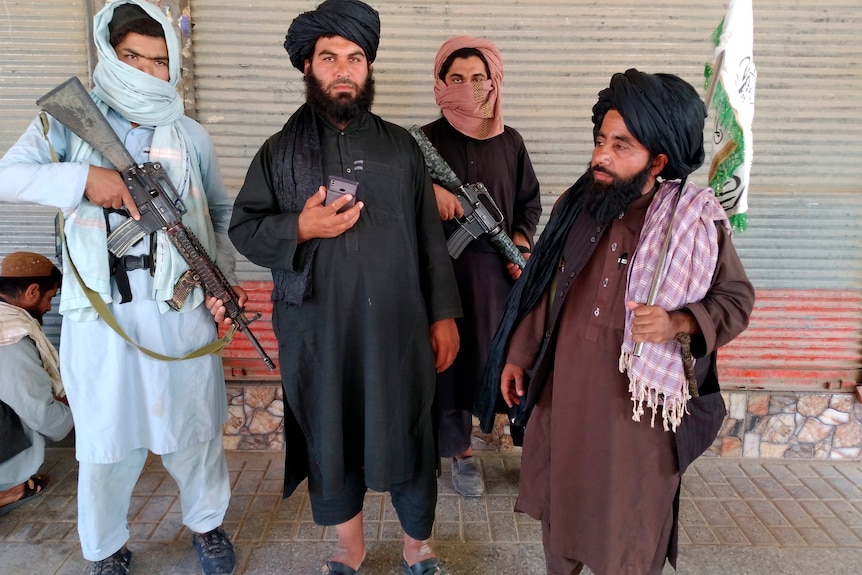 A group of Taliban pose for a photo with a wall in the background.