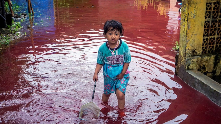 A girl walks through a flooded road with red water