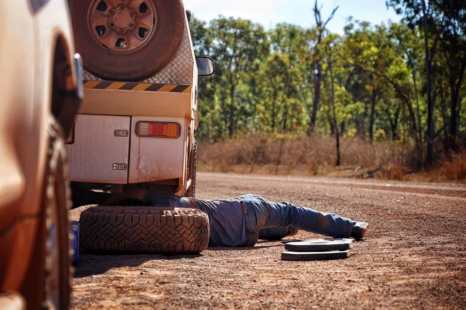 ABC News crew changing flat tyre on car on red dirt road on the way to Gulkula, NT.