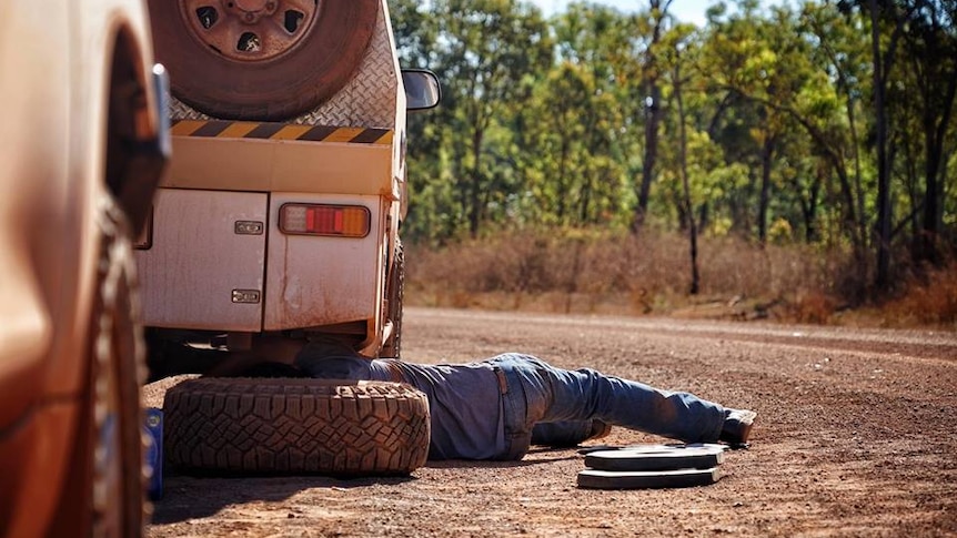 ABC News crew changing flat tyre on car on red dirt road on the way to Gulkula, NT.