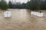 Two rows of large white boxes sitting in brown floodwaters