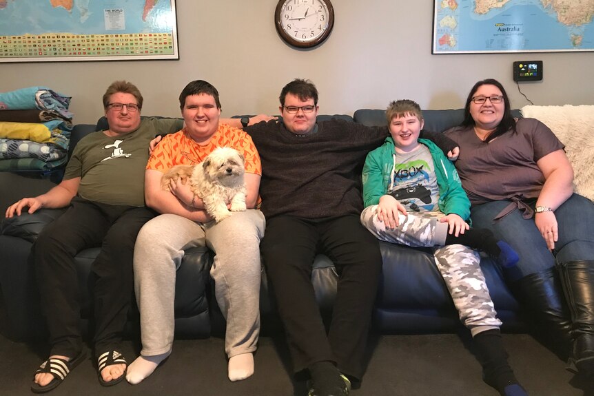 a family of 5 sit on a couch with a white fluffy dog.