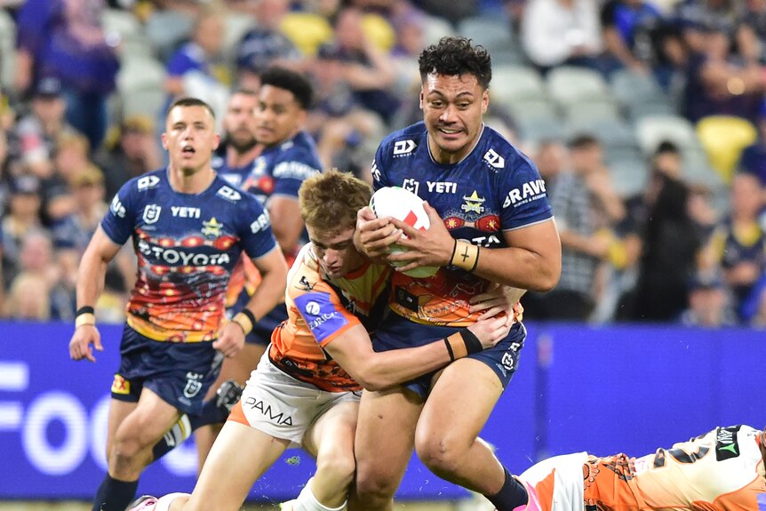 NRL player Jeremiah Nanai running with the football, with two defenders trying to tackle him 
