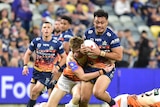 NRL player Jeremiah Nanai running with the football, with two defenders trying to tackle him 