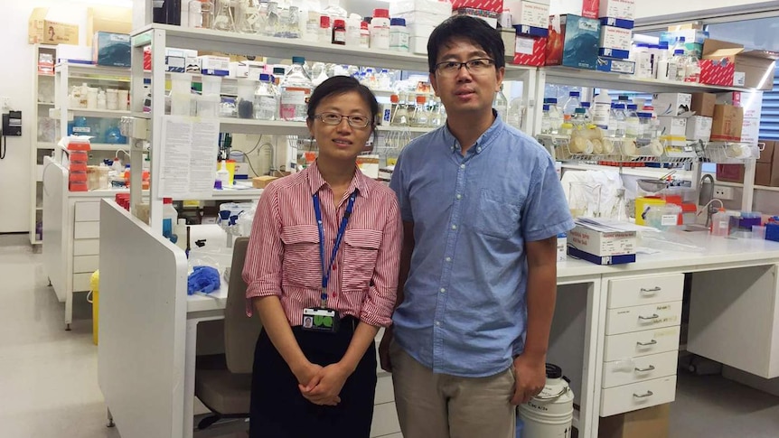 Dr Min Jim and Dr Jianhua Guo stand in front of shelves of bottles and equipment in their laboratory.