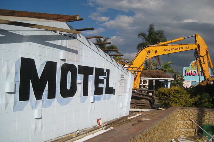 old motel wall, exposed roof beams and an empty pool with crane in the process of demolishing the building
